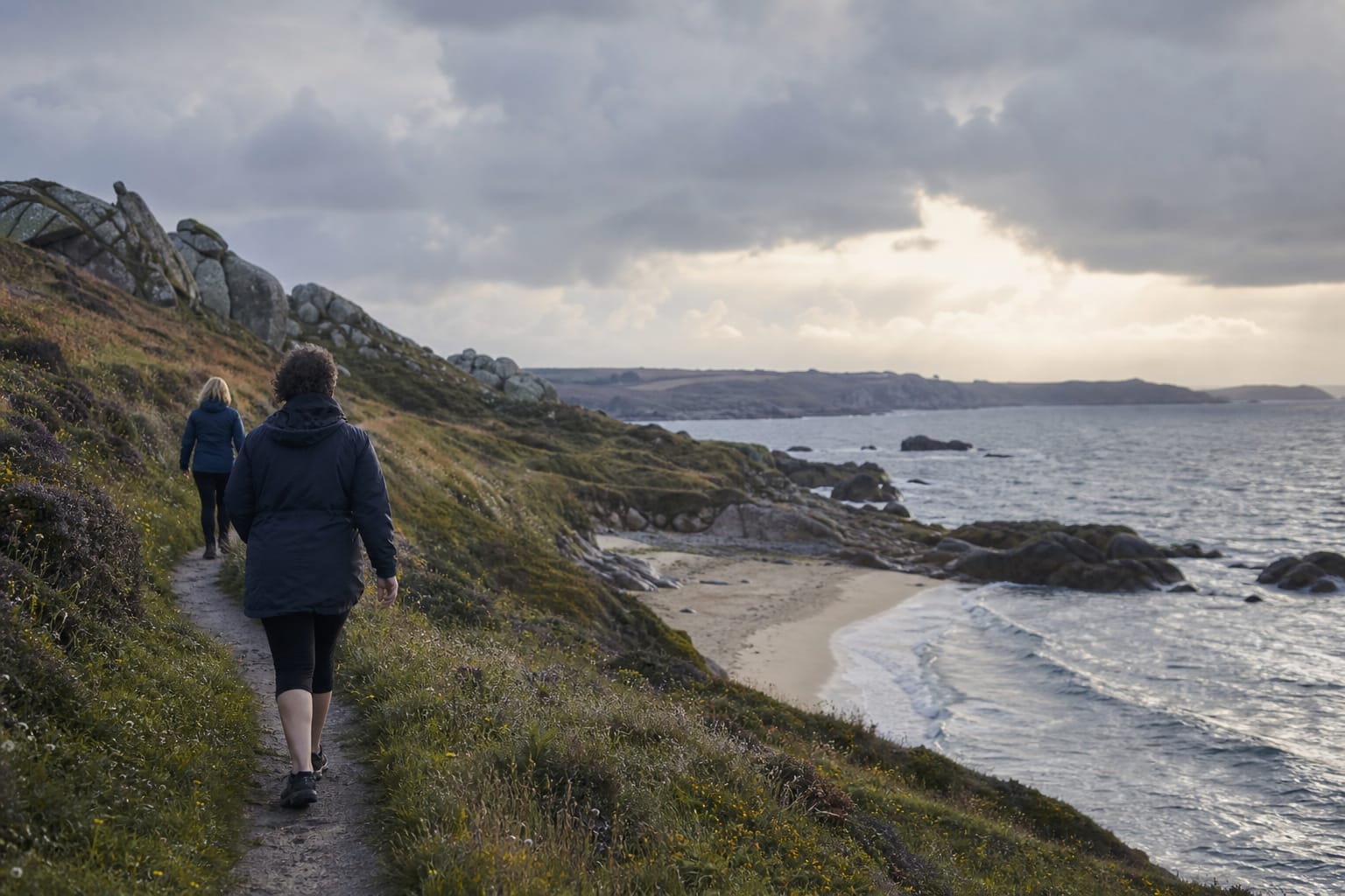 Sentier côtier au-dessus d'une crique de sable clair en Bretagne, fin de journée